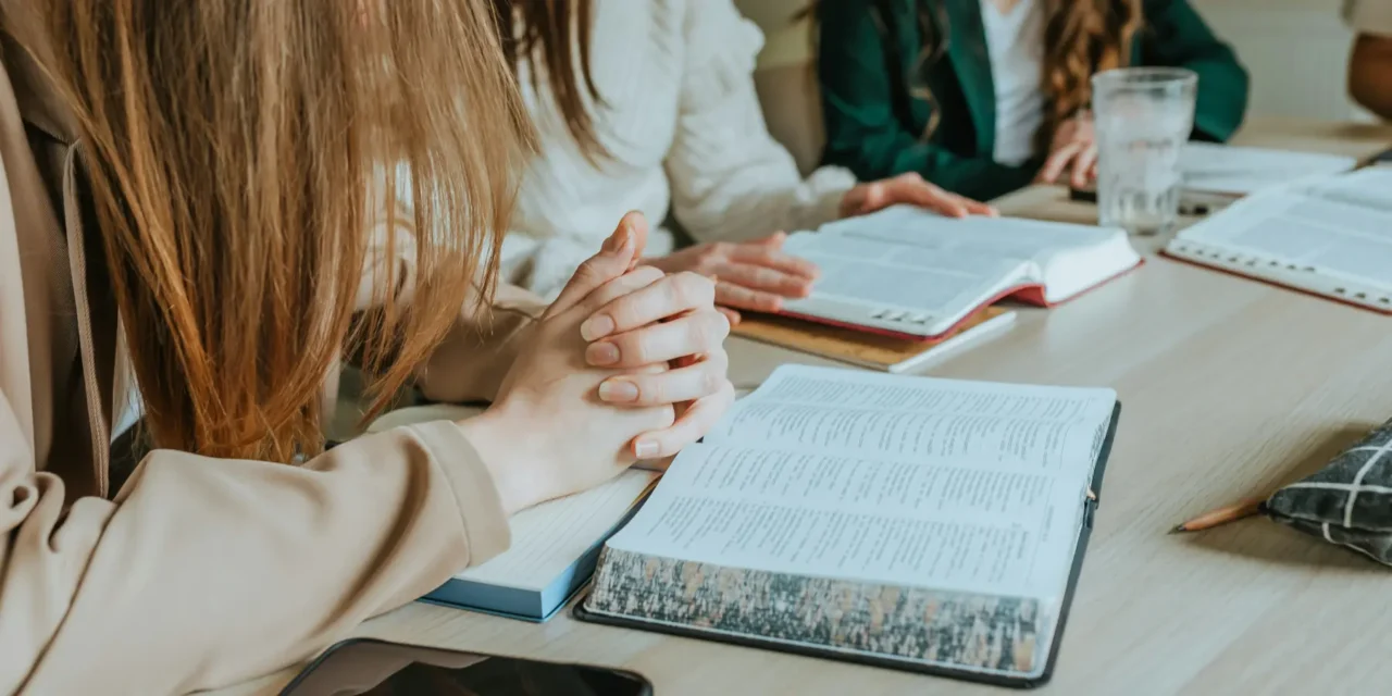 Group of people praying and studying Scripture using monthly Bible study guides at a table